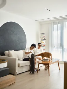 A modern interior design living room featuring a white couch, a wooden coffee table, and two people playing with cats.