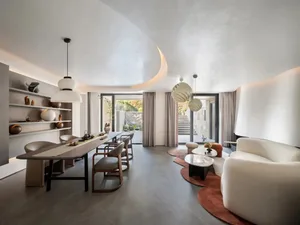 A modern living room with a white sofa, geometric pendant lights, and a long dining table with chairs.