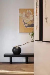 現代客廳內擺放黑色牆邊櫃，黑色花瓶插著樹枝，牆上掛有裱框藝術作品。
