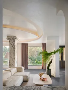 A modern living room with white marble furniture, large windows, and a large potted plant.