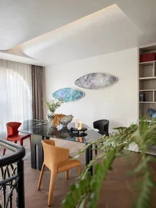 A modern minimalist dining room with a metallic marble table, colorful chairs, and abstract wall art.