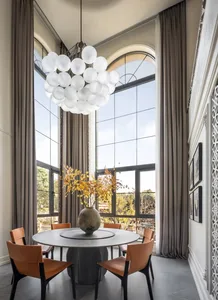 A modern dining room featuring a minimalist design with white lighting, round table, and leather chairs.