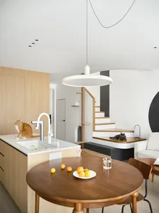A modern minimalist kitchen featuring wooden cabinets, a stainless steel sink, and a round wooden dining table.
