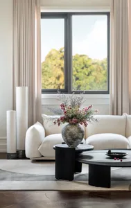 A modern minimalist living room featuring a white sofa, black tables, and a vase of flowers.