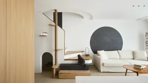 A minimalist living room with wood elements, featuring a white sofa, a black circular wall element, and a cat sitting on a wo