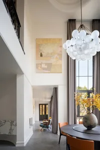 An elegant dining room with modern elements, featuring a marble table, acrylic chairs, and a concrete floor.