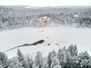 Aerial view of a snow-covered residential house nestled in a frozen forest.