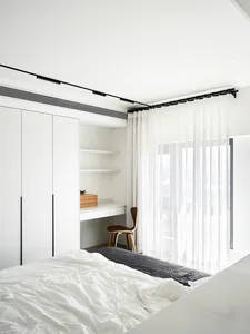 A minimalistic bedroom with a bed, sheer curtains, and a desk.