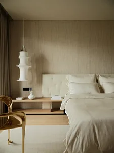 A minimalist bedroom featuring a textured wall, wooden floor, and a leather headboard.