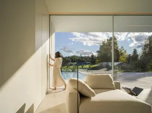 A minimalist living room with a large glass window, a white sofa, and a concrete floor.