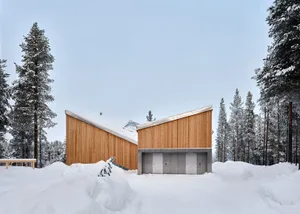 Modern minimalist residential exterior covered in wooden siding with snow-covered ground and surrounding trees.
