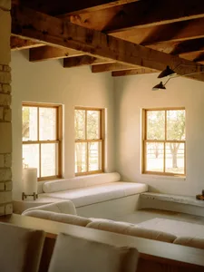 A modern living room featuring comfortable seating with natural fiber upholstery, large windows, and wooden beams under a slo