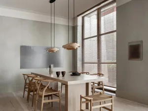 A modern dining room with a wooden table and chairs, featuring tall windows with wooden blinds and minimalist decor.