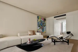 A modern living room with a neutral-toned color palette featuring a white sofa, abstract painting, and black coffee table wit
