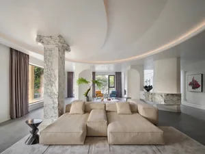 A luxurious living room featuring a marble column, a large beige sectional sofa, and minimalistic decor.