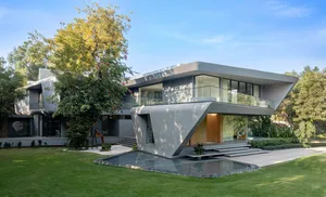 A modern, minimalist house with a concrete exterior and large glass windows, surrounded by greenery.