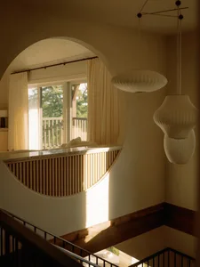 Modern minimalist living room featuring hardwood flooring and a large window with white curtains and pendant lighting