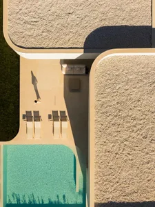 A modern minimalist patio area featuring a concrete floor and gravel accents, with a pool and outdoor seating.