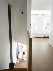 A modern residential interior featuring a white staircase with wood steps, a white sofa, and a minimalist bedroom with white 
