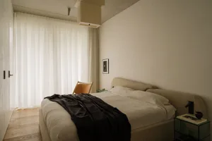 現代極簡臥室，搭配布料床、皮革椅與白色窗簾。