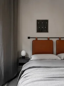 A minimalist bedroom with a brown-leather headboard, light gray bedding, and a gray curtain.