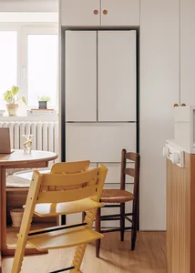 A minimalist kitchen with white laminate cabinets and wooden accents, featuring a round dining table and chairs, plants on th