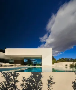 A minimalist white concrete villa with a large swimming pool and glass doors.