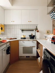 A modern, minimalist kitchen with white cabinets and a wooden floor.