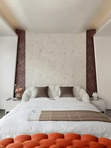 A modern bedroom featuring a bed with white and orange textiles, geometric patterns on the wall, and two white nightstands.
