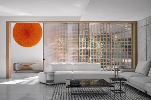 A modern living room with concrete walls, minimalist furniture, and a large, round orange artwork hanging on the wall.