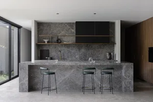 A modern kitchen with a marble countertop, bar stools, and dark cabinets.