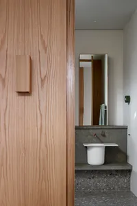 Modern minimalist bathroom featuring a sleek, white sink with a concrete countertop and a tall, rectangular mirror above it.