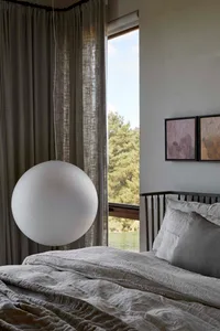 A minimalist bedroom with a white textured glass light sphere hanging above a grey bed.