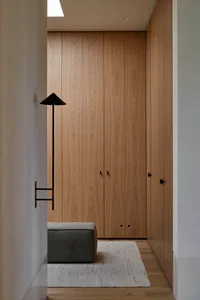 Modern minimalist closet with wood panels and a small ottoman on a white rug.