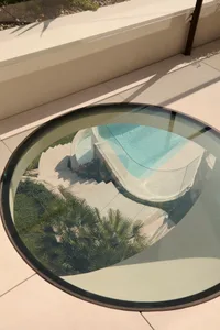 A modern outdoor space featuring a circular glass table with a view of a pool and steps.