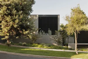 A modern residential house featuring concrete exterior and lush greenery.