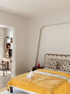 A minimalist bedroom featuring a yellow bedspread and dotted pillow, with a small table nightstand beside the bed.