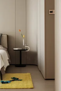 Minimalist bedroom with a yellow rug, wooden floor, and upholstered bed.