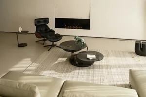 A minimalist living room featuring a modern black lounge chair, round black tables with books and figurines, a beige sofa, an