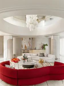 A modern living room featuring a red sofa and a white couch under a white ceiling with a unique light fixture.