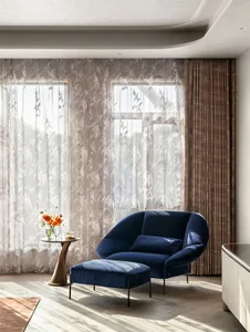 Modern living room featuring a navy blue velvet couch, glass curtains with a floral design, and a minimalist white floor.