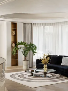A modern living room with a wooden floor, a black sofa, and a circular coffee table with a plant and a vase.