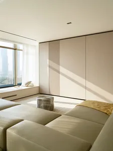 Modern minimalist living room with light wood furniture, leather ottoman, and large windows.