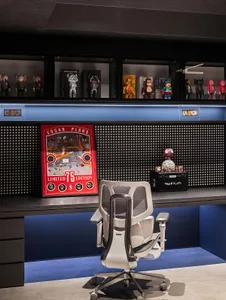 A modern office space featuring a sleek white office chair, a black desk with framed artwork, and a wall-mounted shelf displa