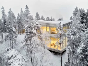 Modern glass house nestled in a snowy winter landscape.