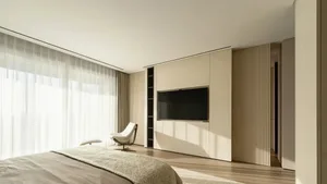 A minimalist bedroom with a large window, white bedding, and a white chair next to a large wooden cabinet.