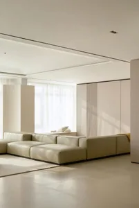 A modern minimalist living room with a large beige sectional sofa and a light-colored rug, featuring soft, neutral tones and 