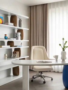 A minimalist workspace with concrete materials, featuring a white desk, an off-white ribbed chair, and a white bookshelf.