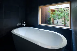 A modern black bathroom interior with a white bathtub and a window view of a tree.