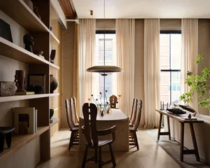 A modern dining room featuring natural wood chairs and a stone table, with a hanging pendant light and large windows with cre
